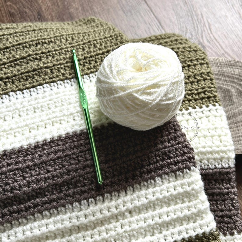 The finished baby blanket, made from this crochet pattern, is lying on a wooden board with a ball of yarn and a crochet hook.