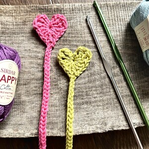 The finished bookmarks, made from this crochet pattern, are lying on a board with yarn and crochet hooks.