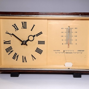 Puede incluir: Un reloj y un termómetro vintage con marco de madera, con una esfera de reloj con números romanos y un termómetro con escala Fahrenheit. El termómetro marca 20 grados Fahrenheit.