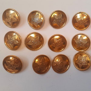 Może przedstawiać: Dwunastu złotych metalowych guzików z pięcioramiennym wzorem gwiazdy. Każda gwiazda ma mniejszą gwiazdę w środku.