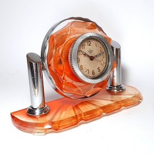 May include: Orange and chrome Art Deco desk clock with a face that reads "12, 1, 2, 3, 4, 5, 6, 7, 8, 9, 10, 11"