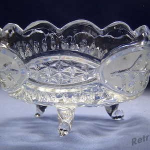 May include: A clear glass bowl with a scalloped edge and a geometric pattern. The bowl has three legs and is ideal for serving snacks or desserts.