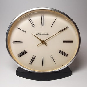 May include: A vintage Molnija clock with a cream-colored face, black Roman numerals, and gold hands. The clock has a silver-colored bezel and sits on a black base. The word "Molnija" is written in cursive on the face.