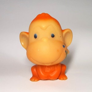 Puede incluir: Juguete de mono de goma naranja con ojos azules y una pequeña flor en la oreja.