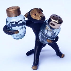 以下が含まれることがあります： 2つのガラスシェーカーを持つブロンズ色の猿の置物を使った、気まぐれな塩コショウ入れセット。猿の顔とシェーカーの蓋は金色の仕上げです。ガラスシェーカーは、テクスチャードデザインの透明です。