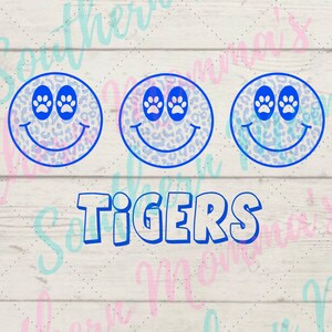 May include: Three blue smiley faces with paw print eyes on a white wood background. The word "TIGERS" is written in blue below the smiley faces.