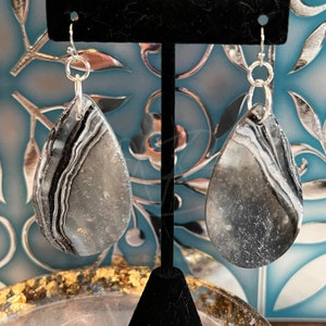 May include: A pair of silver teardrop earrings with black and white agate stone accents. The stones have a sparkly, glittery finish.
