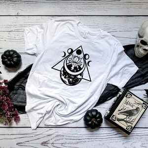 May include: White t-shirt with a black graphic design of a moon, a flower, and a triangle. The design is centered on the shirt.
