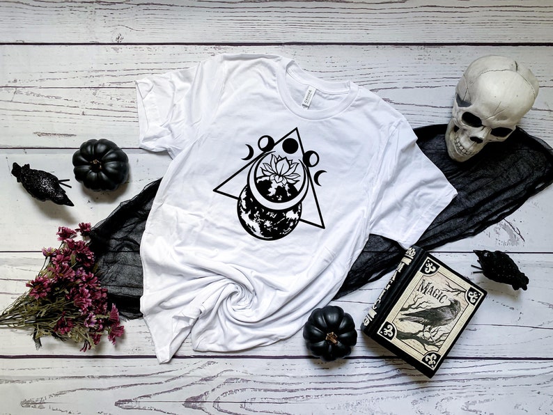 May include: White t-shirt with a black graphic design of a moon, a flower, and a triangle. The design is centered on the shirt.