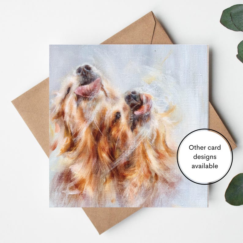 Op de afbeelding: Vierkante wenskaart met een artistieke schildering van twee golden retriever honden met hun tong uit. De honden hebben lang, vloeiend, lichtbruin haar. De kaart zit op een bruine envelop met de tekst "Other card designs available" in een witte cirkel.