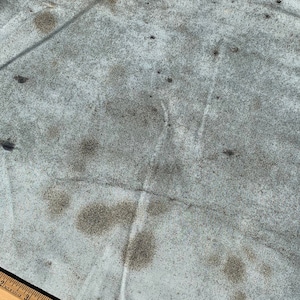 May include: A light blue fabric with dark brown stains and a wooden ruler. The ruler is marked with black numbers and lines, and is 12 inches long. The fabric has a wrinkled texture.