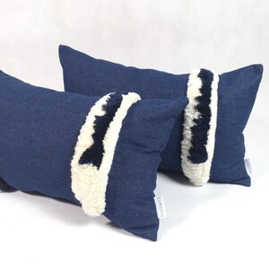 May include: Two blue denim throw pillows with white and black fuzzy trim. The pillows are rectangular and have a subtle texture.