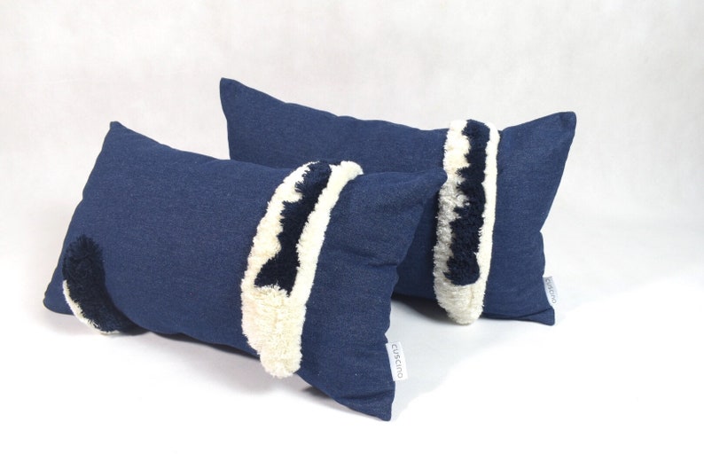May include: Two blue denim throw pillows with white and black fuzzy trim. The pillows are rectangular and have a subtle texture.