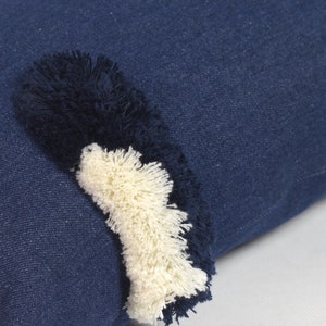 May include: A blue denim pillow with a white and black fringe detail.