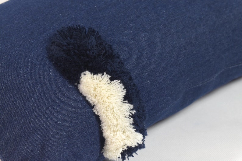 May include: A blue denim pillow with a white and black fringe detail.