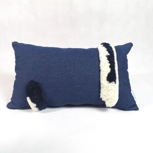 May include: A blue pillow with a white and black fluffy tail and a white and black fluffy stripe on the side.