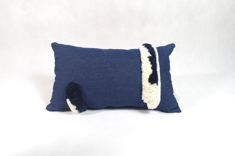 May include: A blue pillow with a white and black fluffy tail and a white and black fluffy stripe on the side.