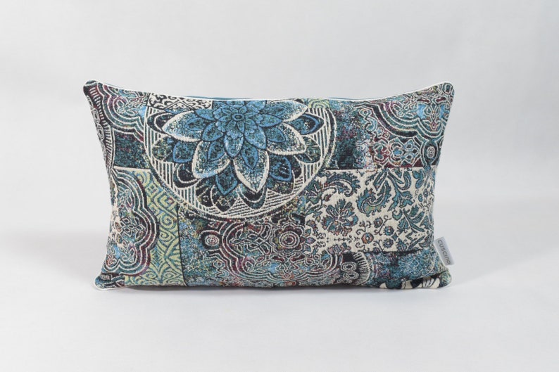 Puede incluir: Una almohada rectangular con un dise&ntilde;o estampado en azul, verde y blanco. El patr&oacute;n presenta un gran motivo floral en el centro.