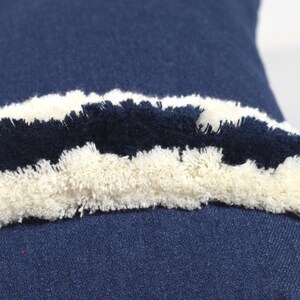 May include: A blue denim pillow with a white and black fringe trim. The fringe is made of fluffy yarn.