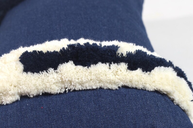 May include: A blue denim pillow with a white and black fringe trim. The fringe is made of fluffy yarn.
