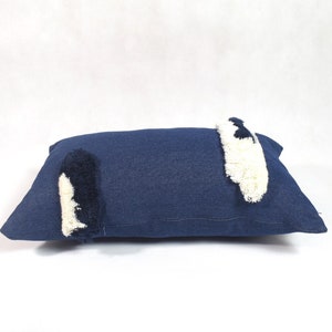 May include: A navy blue rectangular pillow with white and black fringe details.