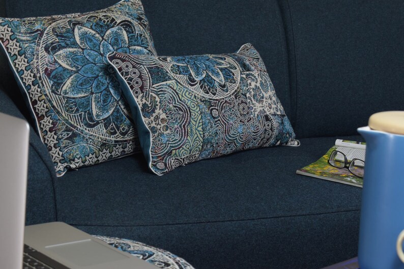 Puede incluir: Dos cojines de tiro azules y blancos con estampado sobre un sof&aacute; azul oscuro. Los cojines tienen un dise&ntilde;o floral y est&aacute;n dispuestos en un sof&aacute; con una revista y una tetera azul a un lado.