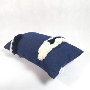 May include: A navy blue throw pillow with white and black pom-poms. The pillow has a white label with the word "cushioned" on it.