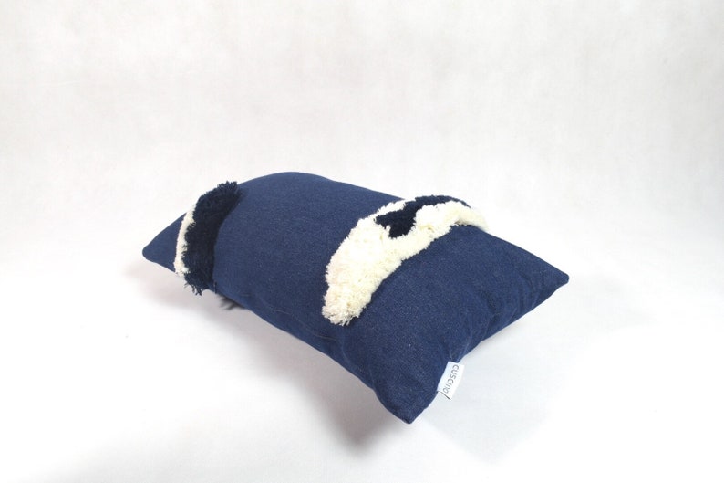 May include: A navy blue throw pillow with white and black pom-poms. The pillow has a white label with the word "cushioned" on it.