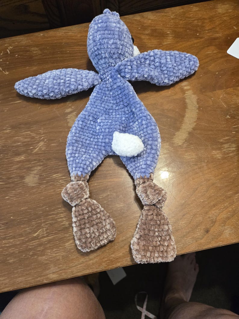 K&ouml;nnte beinhalten: Ein handgefertigtes Pl&uuml;sch-Hasenspielzeug in Blau- und Braunt&ouml;nen. Der Hase hat lange Ohren, einen wei&szlig;en Schwanz und braune F&uuml;&szlig;e. Das weiche, strukturierte Material verleiht ihm ein kuscheliges Aussehen.