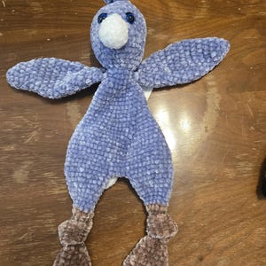 K&ouml;nnte beinhalten: Ein handgefertigtes Pl&uuml;schvogelspielzeug in Blau- und Braunt&ouml;nen. Der Vogel hat einen flauschigen, strukturierten K&ouml;rper, Fl&uuml;gel und Beine. Es hat einen wei&szlig;en Schnabel, blaue Augen und einen kleinen B&uuml;schel blauer Federn auf dem Kopf. Das Spielzeug ist weich und kuschelig.