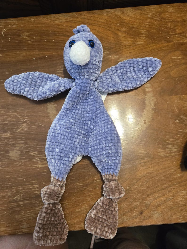 K&ouml;nnte beinhalten: Ein handgefertigtes Pl&uuml;schvogelspielzeug in Blau- und Braunt&ouml;nen. Der Vogel hat einen flauschigen, strukturierten K&ouml;rper, Fl&uuml;gel und Beine. Es hat einen wei&szlig;en Schnabel, blaue Augen und einen kleinen B&uuml;schel blauer Federn auf dem Kopf. Das Spielzeug ist weich und kuschelig.