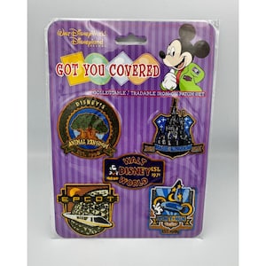 May include: A Walt Disney World and Disneyland Resort collectable iron-on patch set titled Got You Covered. The purple packaging features Mickey Mouse and five embroidered patches representing Animal Kingdom, Magic Kingdom, Walt Disney World, Epcot, and Disney-MGM Studios with their respective establishment years.
