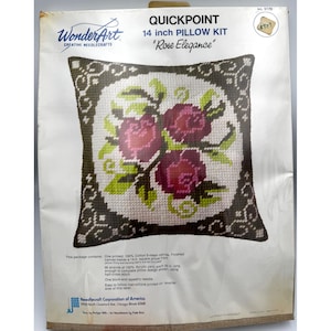 May include: A WonderArt Quickpoint 14 inch pillow kit titled Rose Elegance. The packaging features a graphic of a square pillow with a dark brown border and a central white circle containing three pink roses with green leaves and white scrollwork.