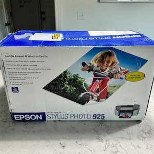 May include: An Epson Stylus Photo 925 ink jet printer box. The box features a photo of a child riding a red bicycle. Text on the box includes "You'll Be Amazed At What You Can Do" and "Photo Lab Image Quality."