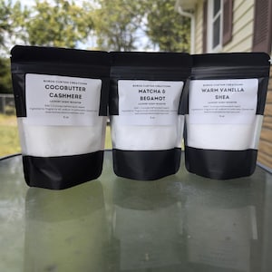 Peut inclure: Trois sachets de poudre blanche pour booster le parfum du linge, dans des sachets noirs et blancs. Les sachets sont étiquetés "Cocobutter Cashmere", "Matcha & Bergamot" et "Warm Vanilla Shea".