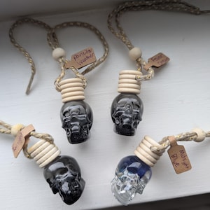 May include: Four skull-shaped car air fresheners with wooden details and braided cords. Each has a different coloured liquid inside. The tags read "Midnight Blue", "Fever Dream", and "Portable Weather".