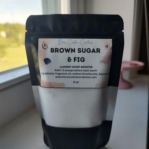 May include: A black pouch of laundry scent booster labelled "Brown Sugar & Fig." The product includes the text "Laundry Scent Booster" and "6 oz." Ingredients include fragrance oil, sodium bicarbonate, and Epsom salt.