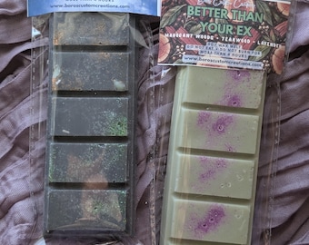 May include: Two rectangular soy wax melt bars in clear plastic packaging. The left bar is dark gray with green glitter, labeled THE NARCISSISTIC MAN. The right bar is light green with purple speckles, labeled BETTER THAN YOUR EX.