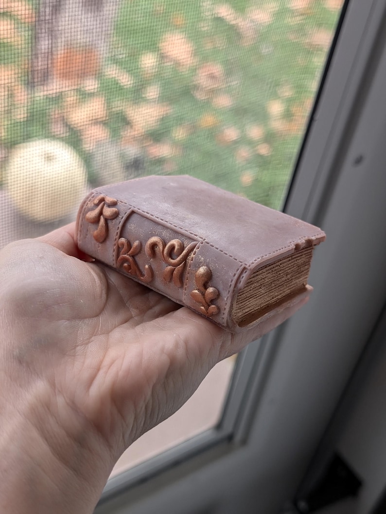 May include: A small, pink book with gold accents and a detailed design. The book is closed and has a worn, vintage look. Book Wax Melt Bookish Decor Book Lover Gift Bookish Wax Melt Cozy Gift for Teacher Booktok Fantasy Lovers Literary Decor Gifts for Readers