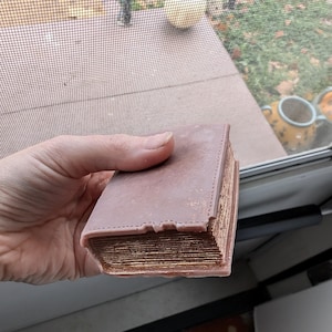 May include: A thick, brown book with gold-colored edges and a textured cover. The book is closed and appears to be very old.
