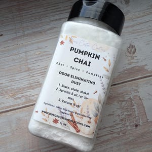 May include: A clear plastic bottle with a black flip-top lid containing white powder. The label reads: Boros Custom Creations, PUMPKIN CHAI, Chai + Spice + Pumpkins, ODOR ELIMINATING DUST, 1. Shake, shake, shake!, 2. Sprinkle & sit for 15+ mins, 3. Vacuum it up!, 283g.