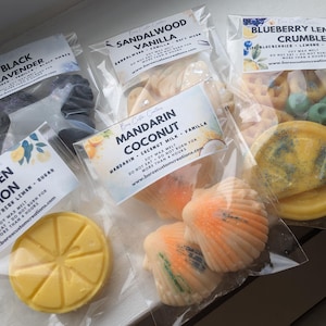 Puede incluir: Cinco bolsas de plástico transparente con ceras aromáticas de soja en diversas formas y aromas. Las fragancias incluyen Black Lavender, Sandalwood Vanilla, Blueberry Lemon Crumble, Mandarin Coconut y Kitchen Lemon, con etiquetas detalladas.