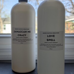 Op de afbeelding: Twee witte plastic flessen vloeibaar wasmiddel met zwarte doppen. Elke fles heeft een etiket met de tekst Boros Custom Creations, de ene gelabeld als Jamaican Me Crazy en de andere als Love Spell, beide met een inhoud van 1065 ml.