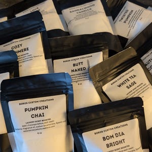 Puede incluir: Un conjunto de bolsas negras y blancas con etiquetas que indican varios aromas. Las etiquetas incluyen "Strawberry Kisses", "Pumpkin Chai", "Cozy Cashmere", "Butt Naked", "White Tea Sage" y "Autumn Cottage". Las bolsas son para potenciadores de aroma para la colada.