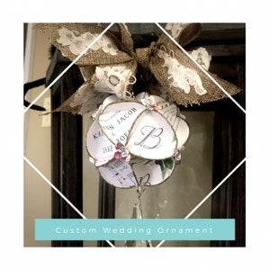 May include: A custom wedding ornament made of paper, featuring a floral design and the couple's names, "Kaitlin & Jacob", and the initial "B". The ornament is decorated with glitter and a crystal teardrop.