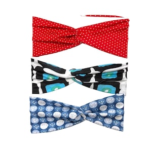 May include: Three fabric headbands in a row. The top headband is red with white polka dots. The middle headband has a black, white, and blue floral pattern. The bottom headband is blue with a white and blue floral pattern.