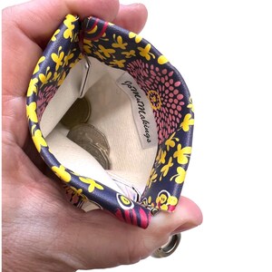 May include: A small zippered pouch with a floral print in shades of pink, yellow, and blue. The pouch is open and has coins inside. The label inside reads "Jo-Mu Makings."