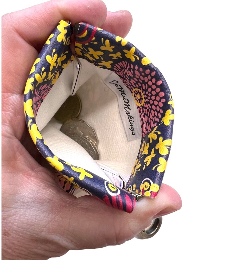 May include: A small zippered pouch with a floral print in shades of pink, yellow, and blue. The pouch is open and has coins inside. The label inside reads "Jo-Mu Makings."