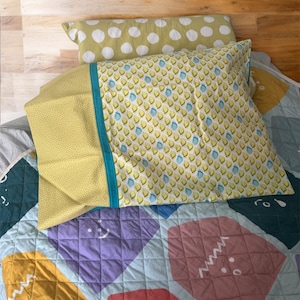 May include: A bed with a patterned quilt and pillows. The pillows have yellow and white polka dots, and a yellow pillowcase with a blue stripe. The quilt has a colorful geometric design with squares and diamonds.