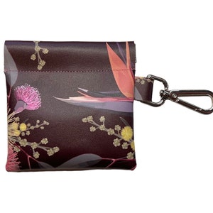 May include: A small, dark brown leather pouch with a floral print featuring pink, yellow, and orange flowers. The pouch has a silver metal clip attached to it.